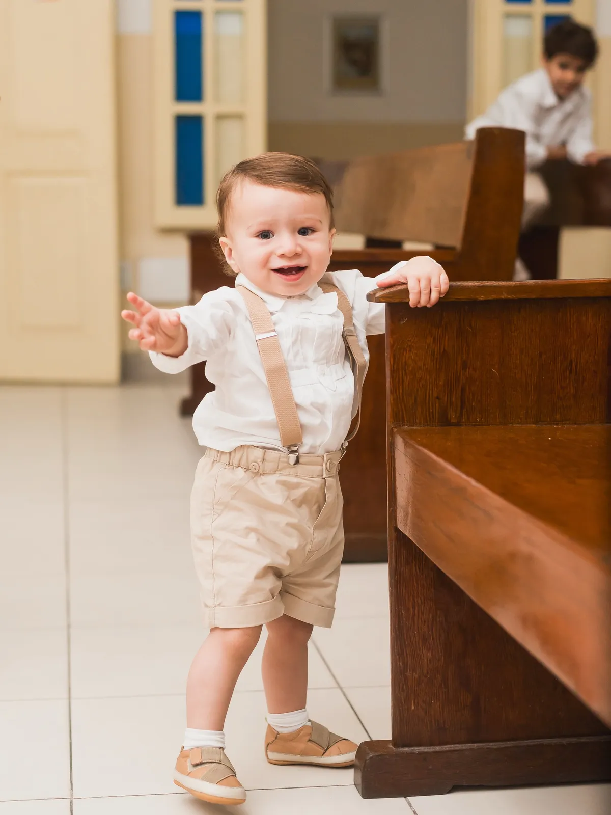 Criança pequena de pé, apoiada num banco de madeira, durante uma celebração.